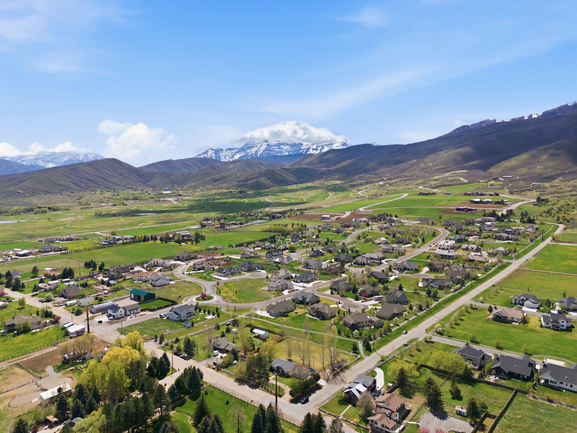 Aerial view of Midway Utah homes with green fields and snow-capped Wasatch Range mountains